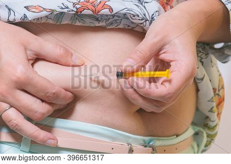 Woman is doing an insulin or heparin injection in her abdomen at home