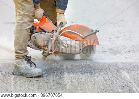 A Worker Repairs A Section Of Road, Cuts Worn Asphalt In A Cloud Of Dust With A Portable Asphalt Cut