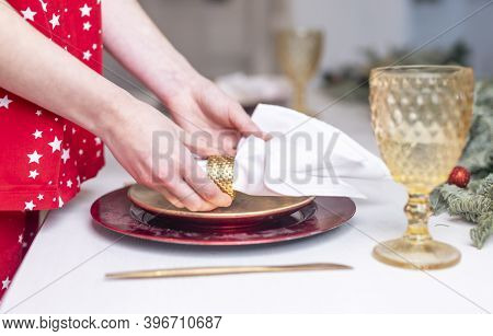 Female Hands Close Up Set The Table For Christmas, Decorating It With White Napkin, Plates And Wineg