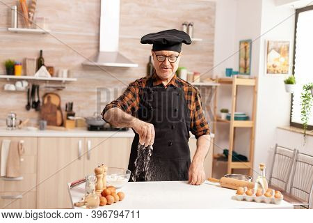 Elderly Baker Preparing Tasty Food Using Bio Wheat Flour Wearing Apron And Bonete. Retired Senior Ch