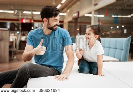 Bearded Handsome Man With Daughter Sitting On Mattress. Choosing Mattress In Store.