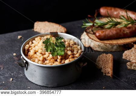 botifarra amb mongetes, fried white beans and sausage, a traditional dish of Catalonia, Spain, served in an old metallic lunch box, on a slate stone surface