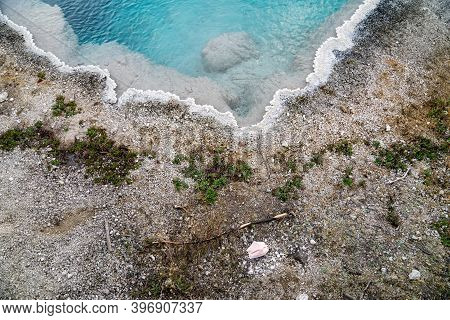 Disgarded, Littered Surgical Face Mask Sitting In The Black Pool, A Hot Spring With Teal Waters In T