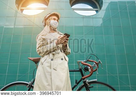 Woman in protective maskin, in helmet using her smartphone device. Female his bike. Girl standing on green background.