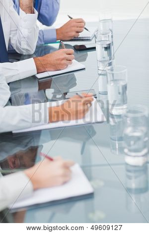 Close up on workmates taking notes while attending presentation in bright office