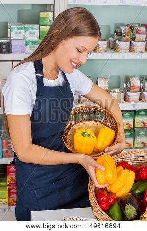 Young saleswoman choosing bellpeppers in grocery store