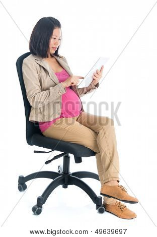 Full body six months pregnant Asian business woman using digital computer tablet pc, sitting on chair isolated on white background.