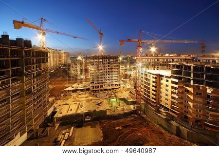 Lots of tower cranes build large residential buildings at night.
