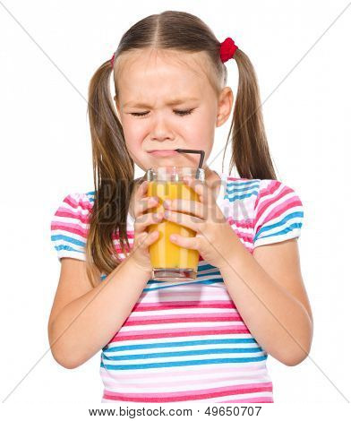 Little girl unwillingly drinking orange juice using straw, isolated over white