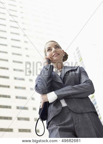 Low angle view of businesswoman conversing mobile phone against tall office building