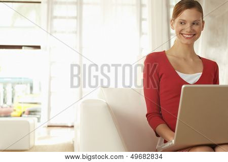 Happy young businesswoman with laptop sitting on chair in office lobby