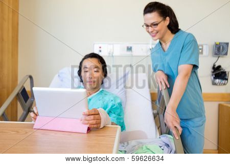 Young nurse and mature male patient looking at digital tablet in hospital room
