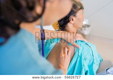 Cropped image of female nurse checking patient's back with stethoscope on bed in hospital