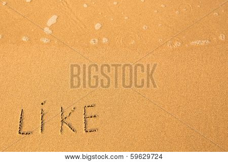 Like - text written by hand in sand on a beach, with a soft wave.