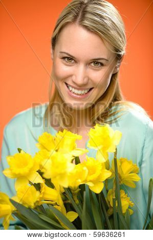 Smiling woman holding yellow narcissus spring flowers on orange background