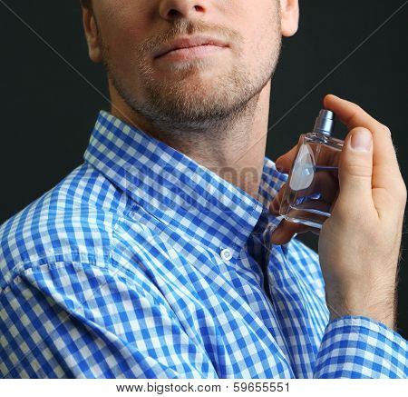 Handsome young man using perfume on black background