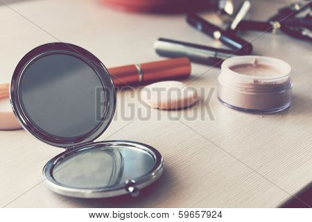 Compact pocket mirror next to powder and a powder puff and other cosmetics
