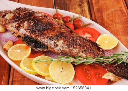healthy lunch : whole fried sea sunfish on wooden table with lemons peppers and tomatoes and rosemary twig