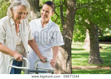 Smiling young female assisting mature woman with walker at the park