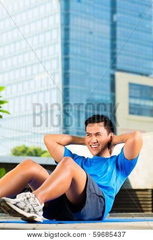 Urban sports - young Asian Indonesian man is doing warming up and sit-ups before running in the city on a beautiful summer day