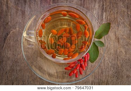 Goji Fresh Antioxidant Tea In Glass Cup And Barberries In Wooden Bowl