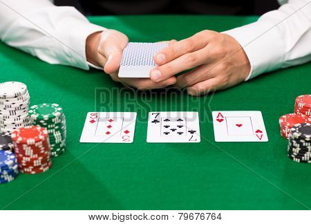 casino, gambling, poker, people and entertainment concept - close up of holdem dealer with playing cards and chips on green table
