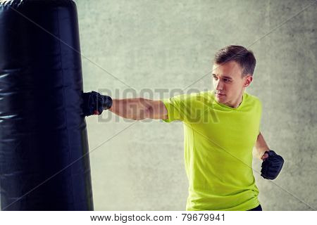 sport, box and people concept - young man in gloves boxing with punching bag in gym
