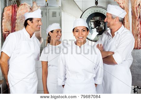 Portrait of confident female butcher with colleagues in butchery