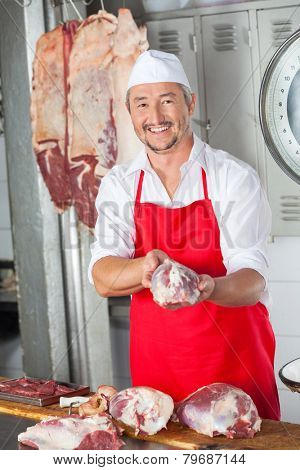 Portrait of smiling mature male butcher holding meat in butchery