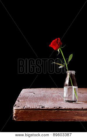 a red rose in a glass vase placed on a rustic wooden table, over a black background
