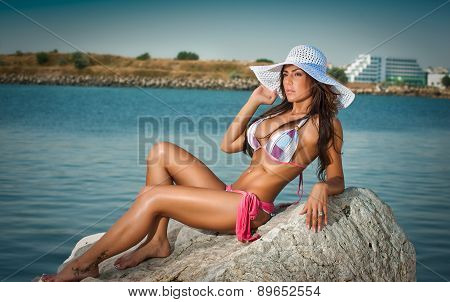 Full length portrait of young sexy brunette girl in bikini and big white hat at the beach