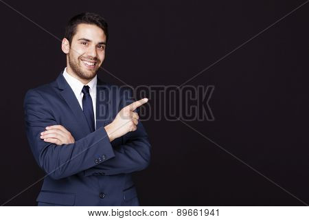 Handsome business man pointing at something against dark background