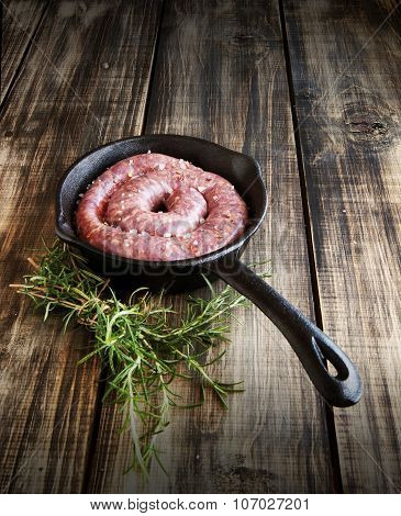raw beef sausages on a cast-iron pan with rosemary and spices,  wooden table, selective focus