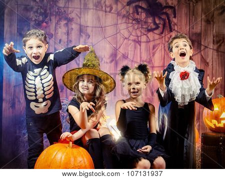 Cheerful children in halloween costumes celebrating halloween in a wooden barn with pumpkins. Halloween concept.