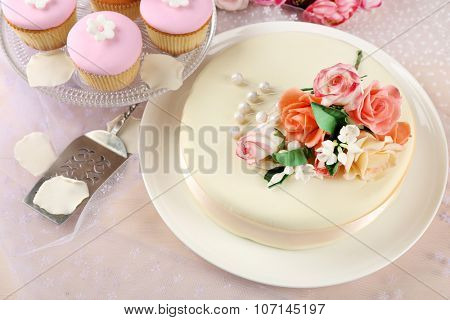 Cake with sugar paste flowers and cupcakes, on light background
