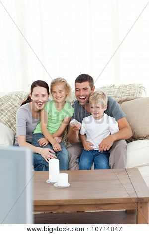Onnellinen perhe nauraa katsoessasi televisiota, istuu sohvalla