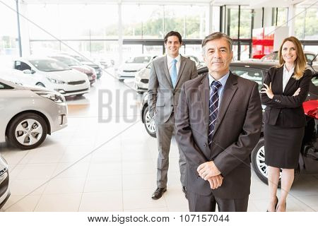 Group of smiling business team standing together at new car showroom