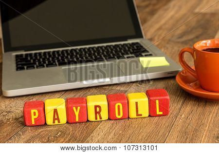 Payroll written on a wooden cube in front of a laptop