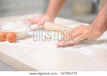 Young male cook is stretching the dough thoroughly.