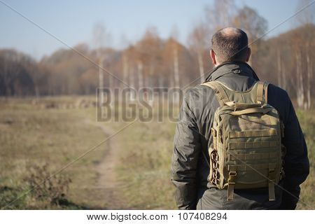 man with a backpack on his shoulders walking on path in park