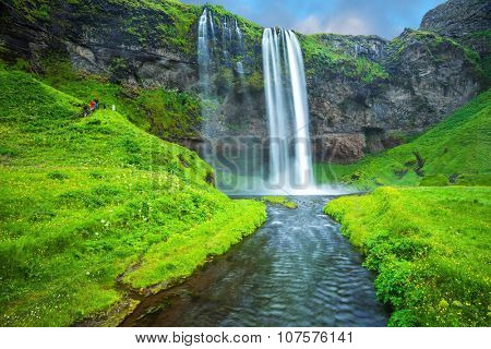 The warm July day in Iceland. Seljalandsfoss waterfall. Rainbow decorates drop of water