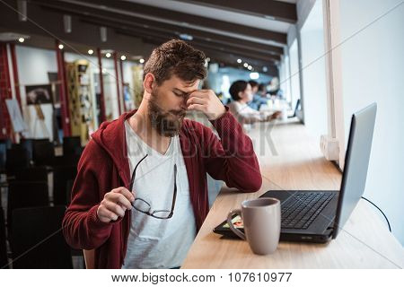 Young handsome exhausted bearded man tired using laptop