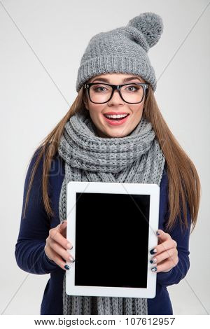 Prtrait of a smiling woman in winter cloth and glasses showing blank tablet computer screen isolated on a white background