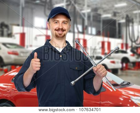 Smiling car mechanic with tire wrench over garage background.