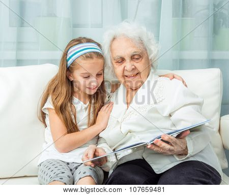 elderly woman with granddaughter with book on sofa