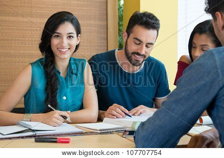 Closeup of young woman looking at camera while studying with her friends at library. Portrait of female student preparing for the exam.Beautiful young woman looking at camera.