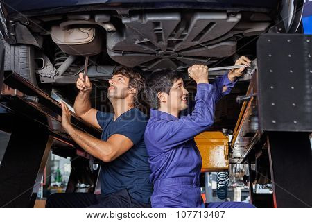 Male mechanics working under lifted car at auto repair shop