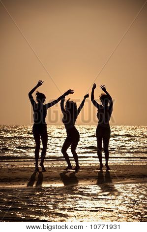 3 หญิงสาวที่เต้นรำบนชายหาดพระอาทิตย์ตกดิน