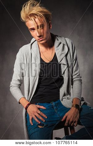 confident man with messy hair posing in sudio while sitting and looking at the camera