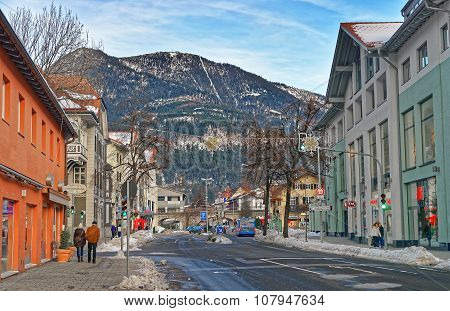 GARMISCH-PARTENKIRCHEN GERMANY - JANUARY 06 2015: Small Alpine town street with typical houses people walking down the street mountains in the background. Garmisch-Partenkirchen Bavaria Germany